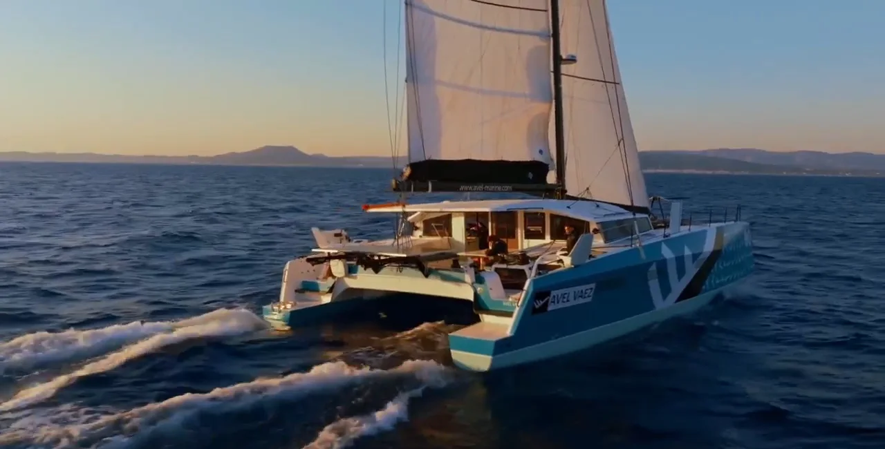 The catamaran AVEL VAEZ under full sail at speed, in low evening sun